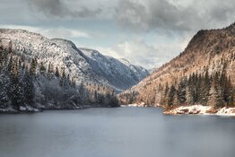 Lake between mountains with snow and pines